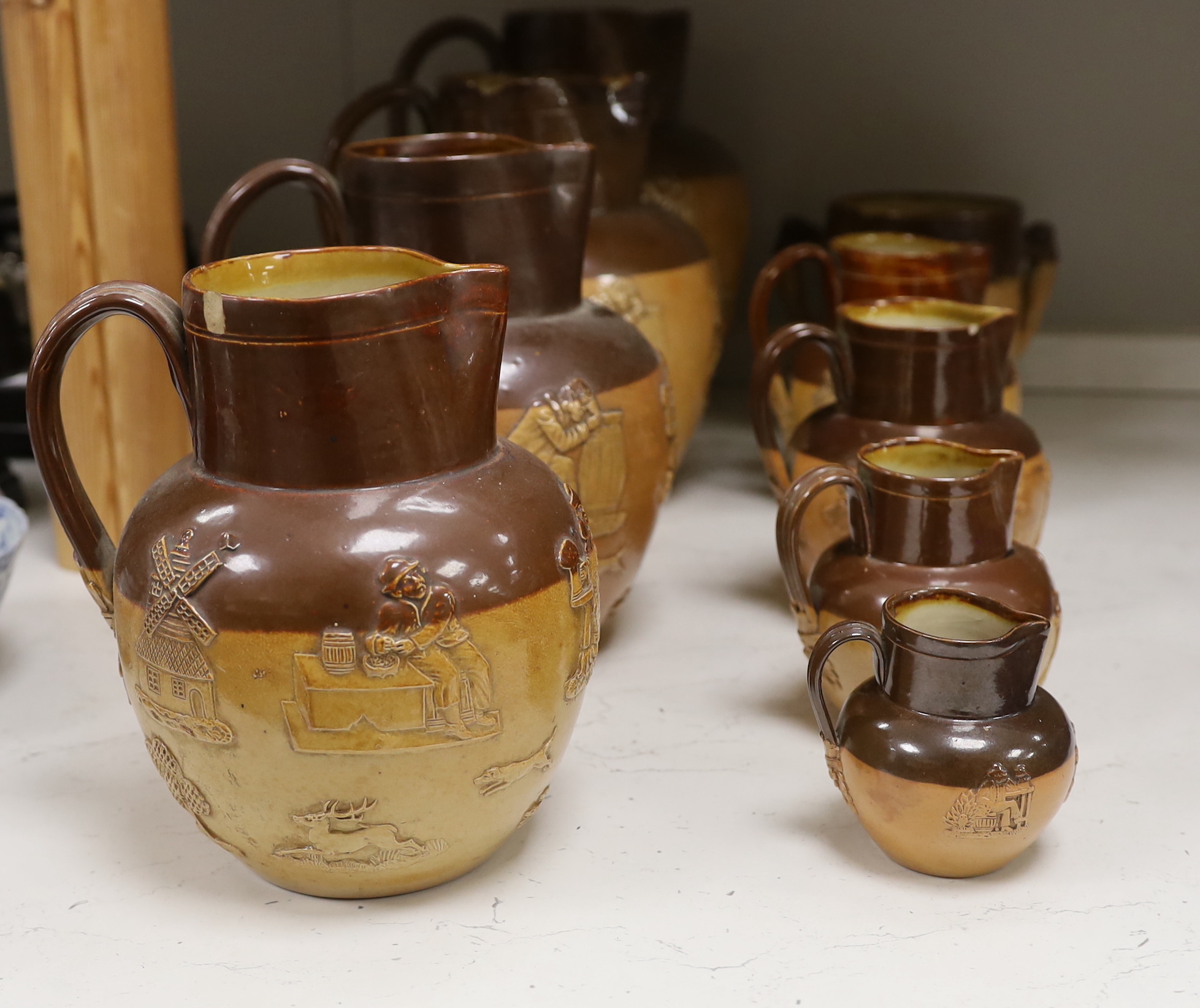 Eight Doulton stoneware jugs and a tyg, largest 27cm high
